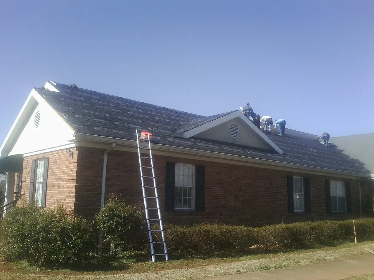 Crew tearing shingles off a brick ranch roof with a ladder set — Emergency Roof Repair work by our crew in New Paris