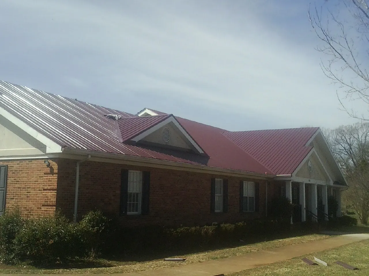 Red metal roof with gabled entries on a long brick building, from a Hail Damage Roof Repair job in New Paris