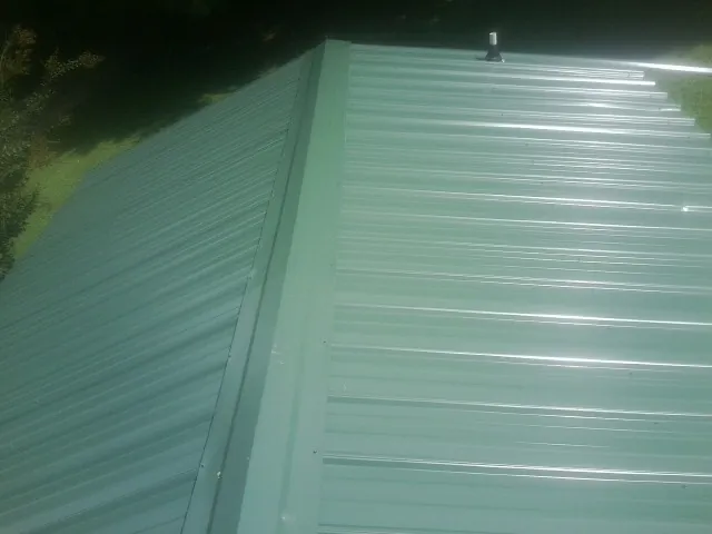 New green metal panels meeting at the ridge of a roof — Flat Roof Repair work by our crew in New Paris