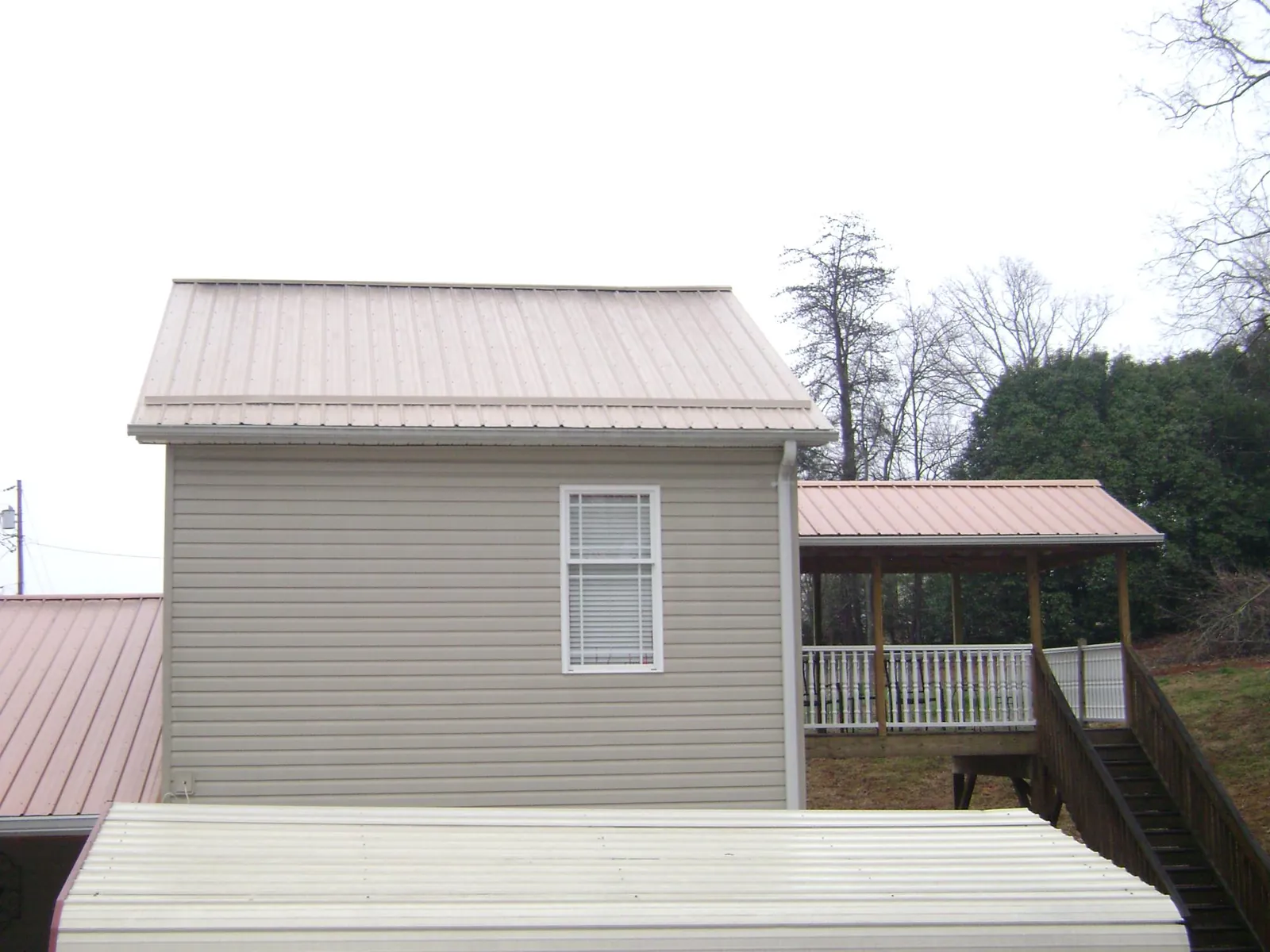 Tan metal roofs on a two story addition and attached porch, from a Roof Replacement job in New Paris